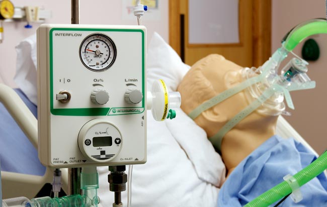 A ventilator in used to support a patient  with their breathing as they lie in a hospital bed