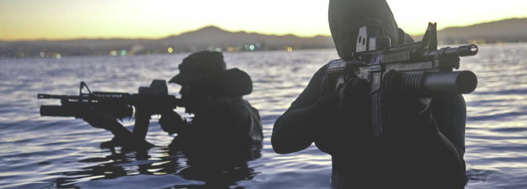 Two armed personnel dressed from head to toe in black standing chest deep in water 