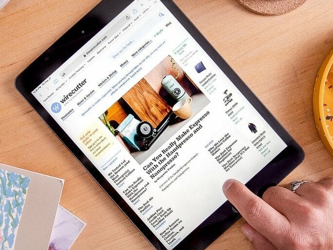A touchscreen tablet sat on a table with a hand on the right hand side touching the screen