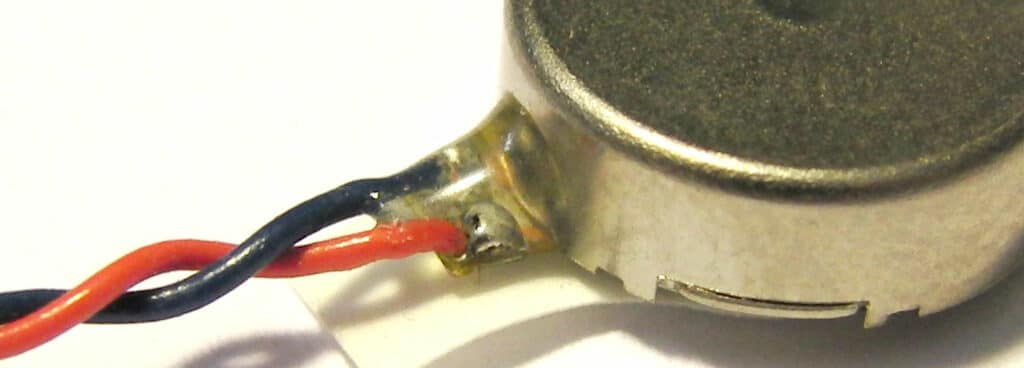 A close-up of a coin vibration motor with leads that are attaching using adhesive