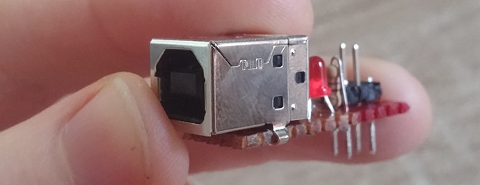 A hand holding a simple circuit board that uses a USB connector and a set of jumpers to connect to the breadboard