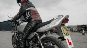 The side view of a biker wearing biker leathers and helmet while sat on motorbike.