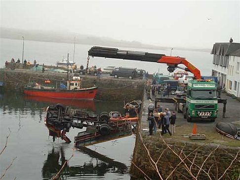 Small crane being lifted out of a harbour by a bigger crane