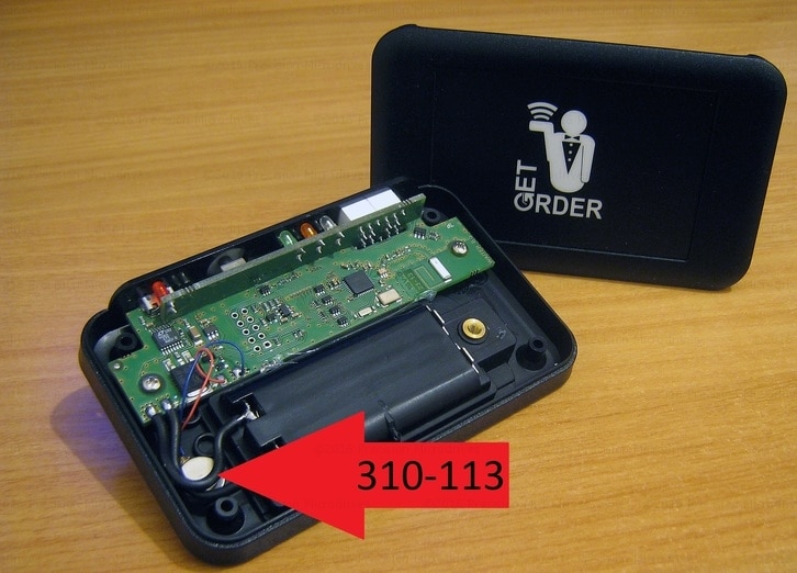 In the foreground a getOrder device that has been opened to show the PCB and there is a red arrow pointing to our 310-113 vibration motor. In the background is the front of the device showing the logo